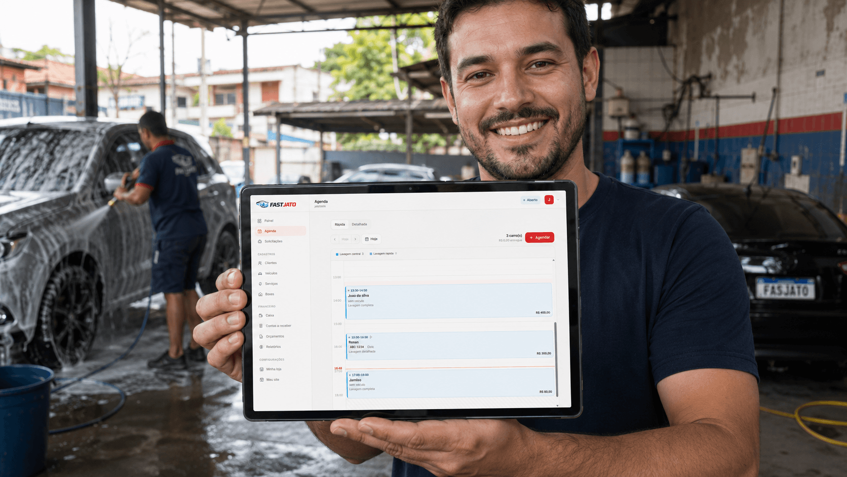 Dono de lava jato segurando um tablet com a agenda do FastJato aberta, com um carro sendo lavado ao fundo